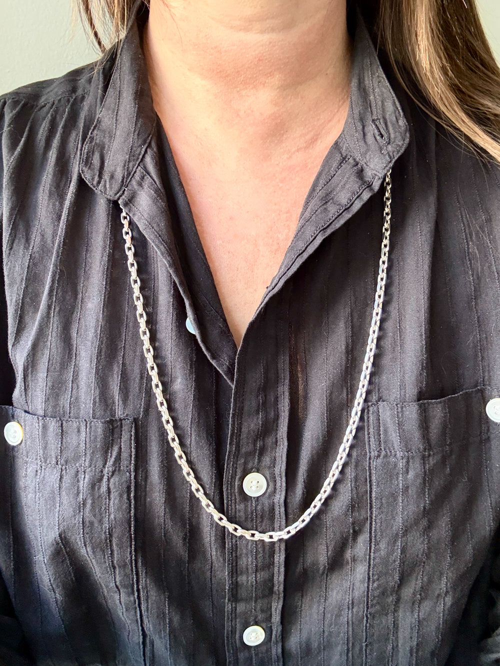 Person wearing a dark gray shirt with a long silver chain necklace.