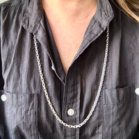 Person wearing a dark gray shirt with a long silver chain necklace.