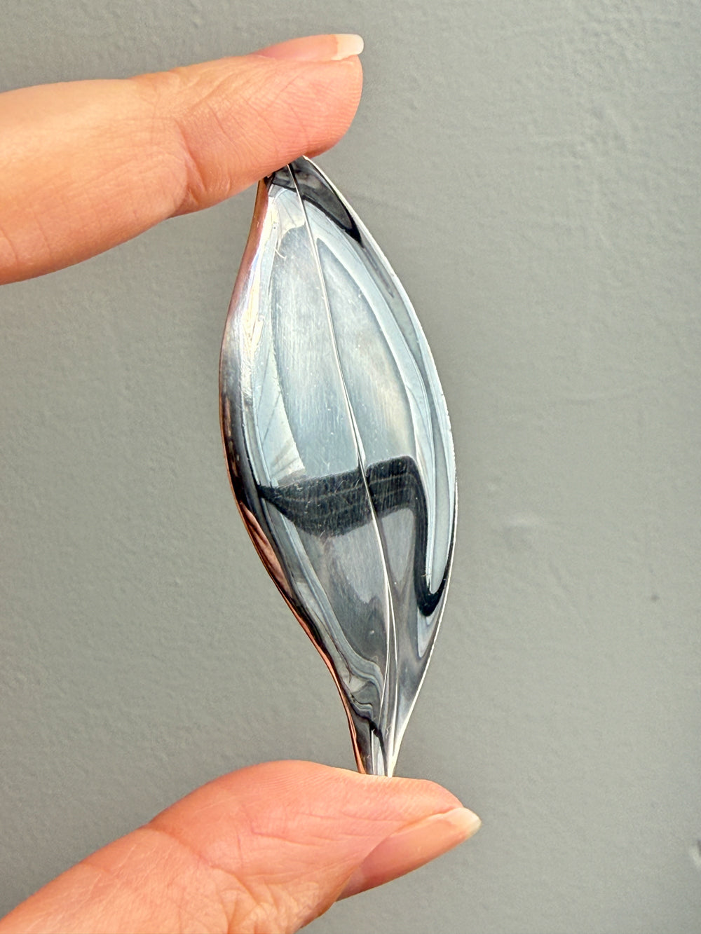 Hand holding a sterling silver leaf shaped brooch against a plain background