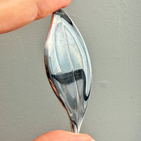 Hand holding a sterling silver leaf shaped brooch against a plain background