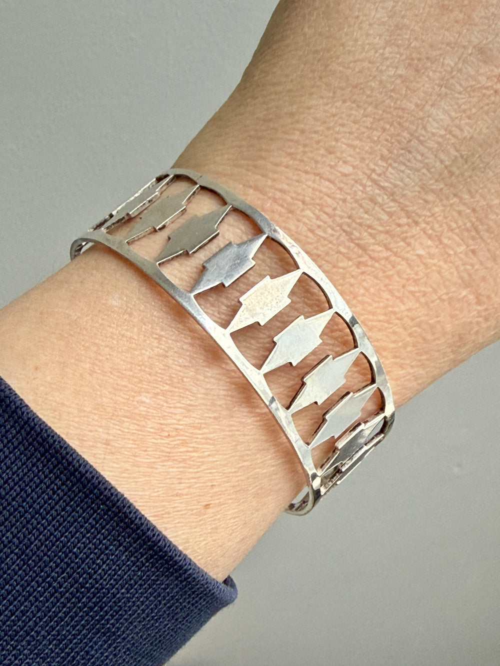 Silver bracelet with cut-out design on a wrist against a neutral background