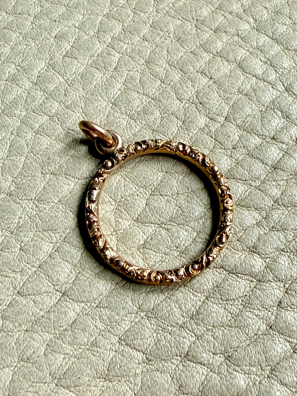 18k Gold ring-shaped pendant on a textured light green background