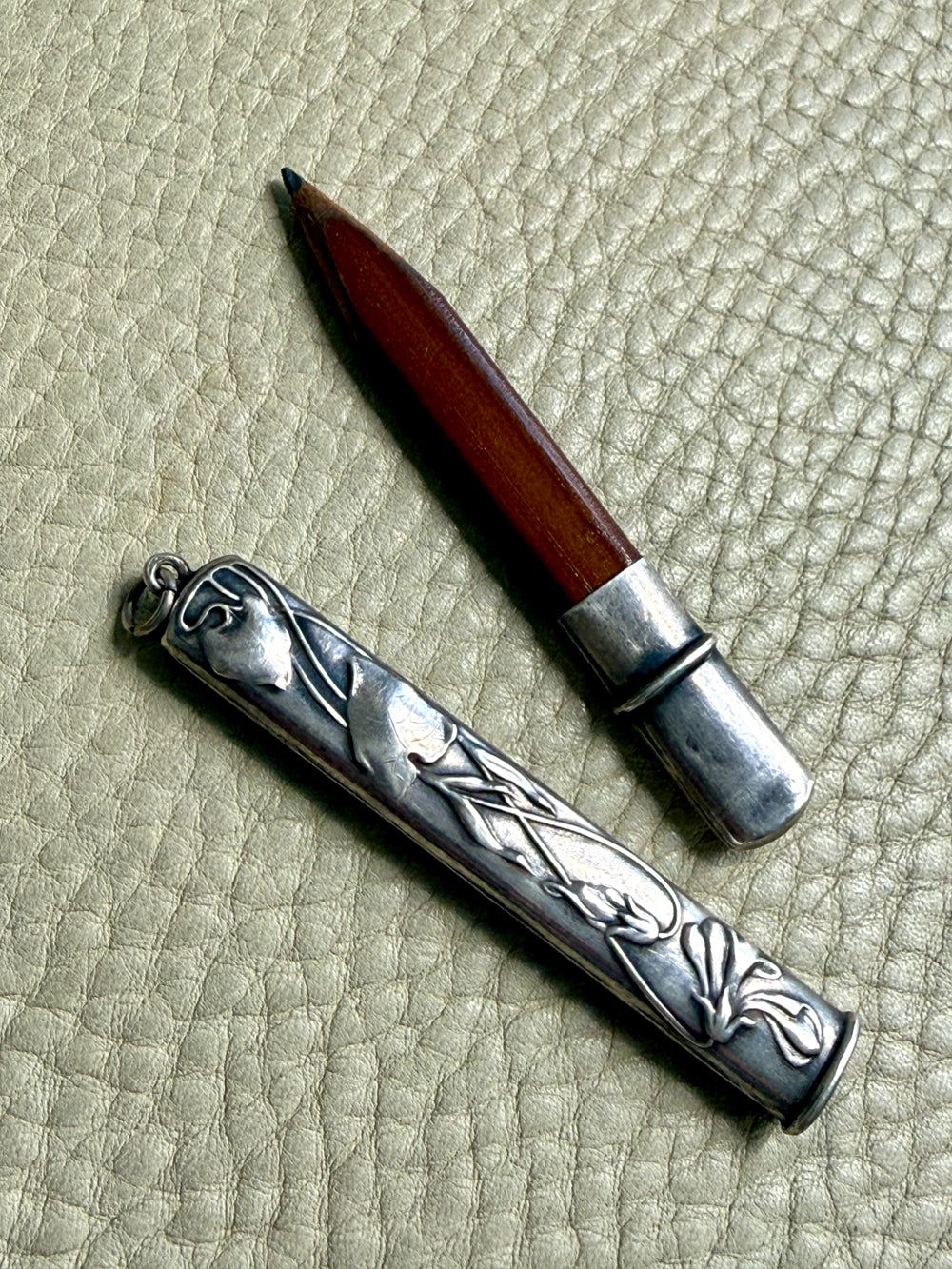 Silver art nouveau pencil case with intricate designs on a textured beige surface