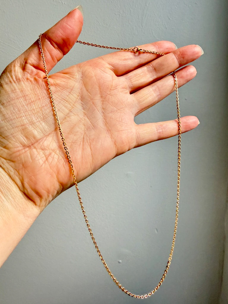 Hand holding a gold chain against a gray background