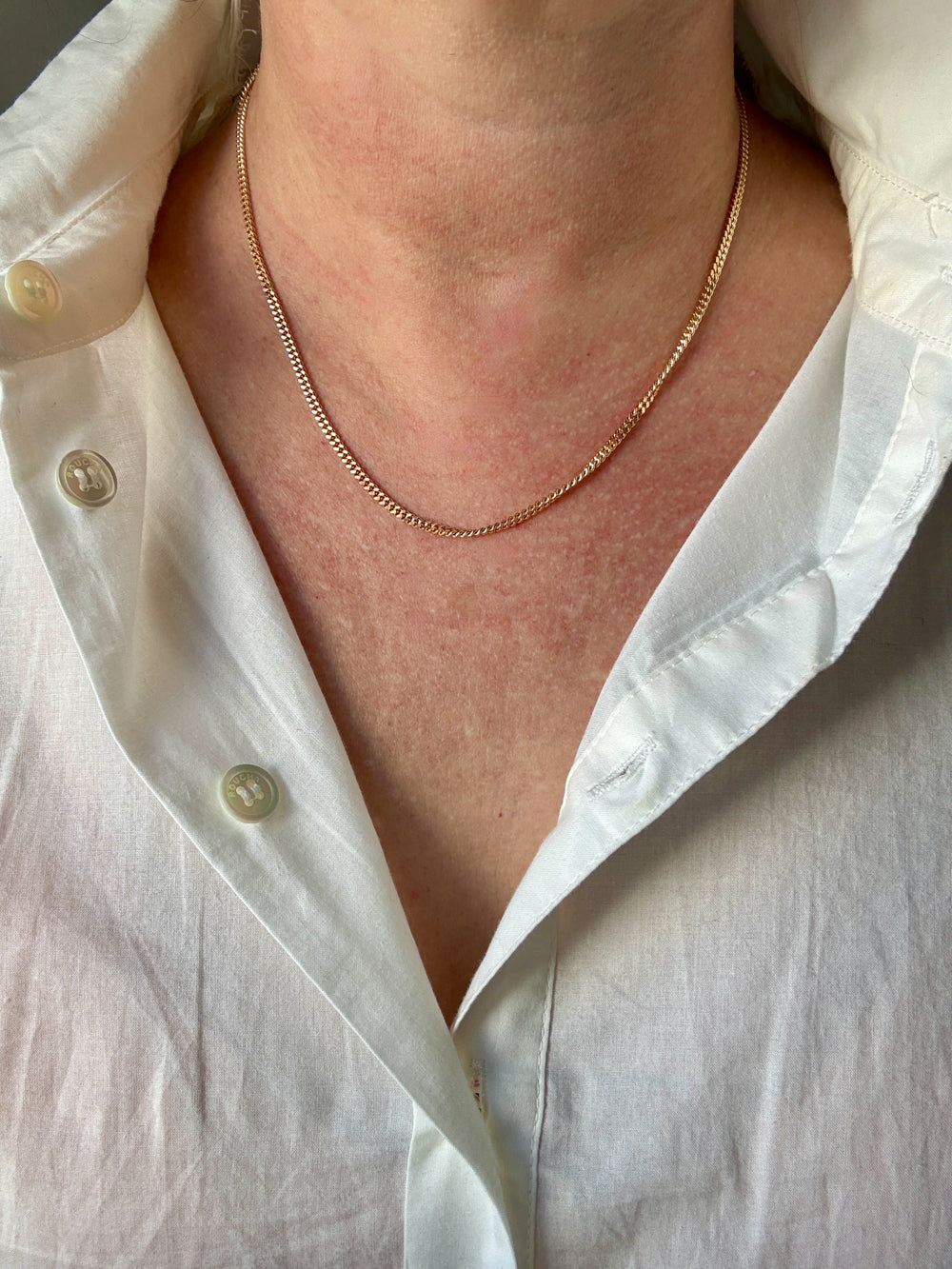 Close-up of a person wearing a gold necklace with a white shirt.