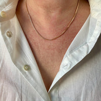 Close-up of a person wearing a gold necklace with a white shirt.