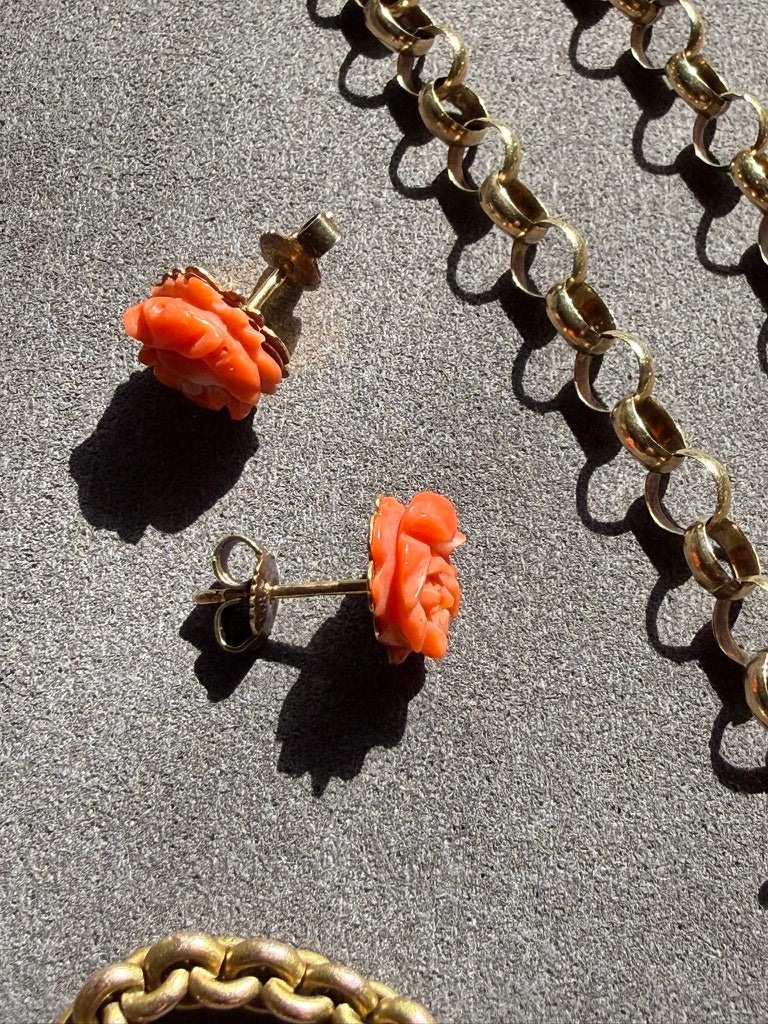 Pair of coral rose earrings on a textured surface with gold chain.