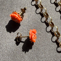 Pair of coral rose earrings on a textured surface with gold chain.