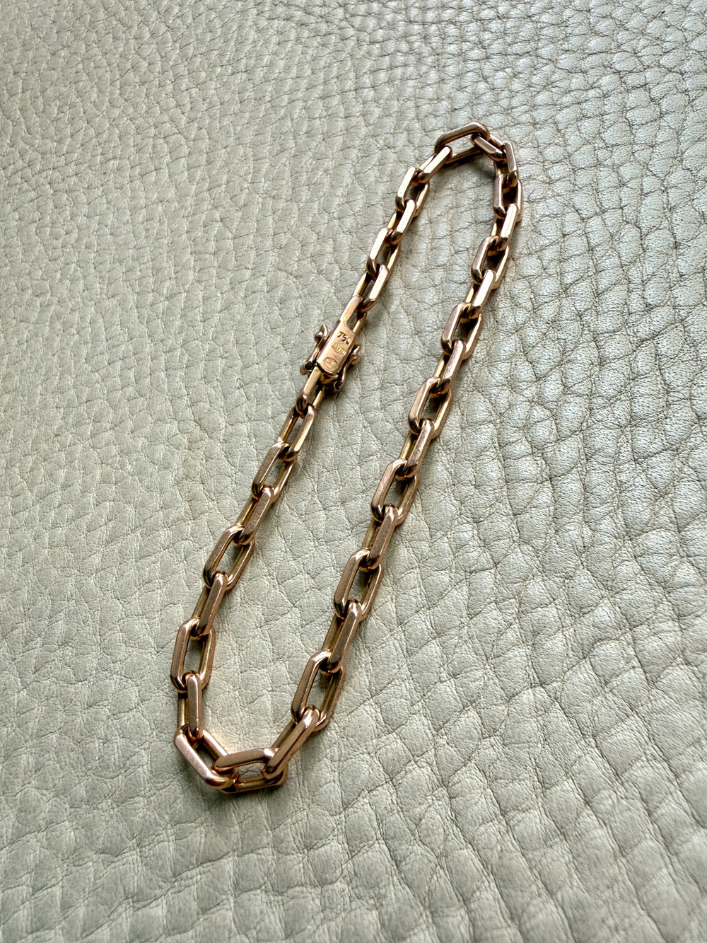 18k Gold chain bracelet on a textured light gray surface