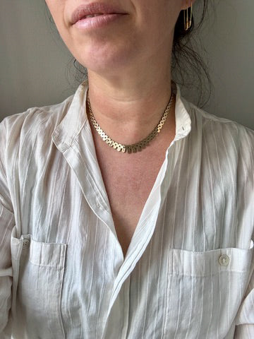 Person wearing a white shirt and gold necklace against a neutral background