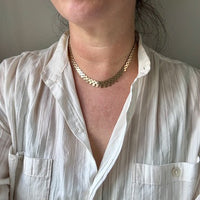 Person wearing a white shirt and gold necklace against a neutral background