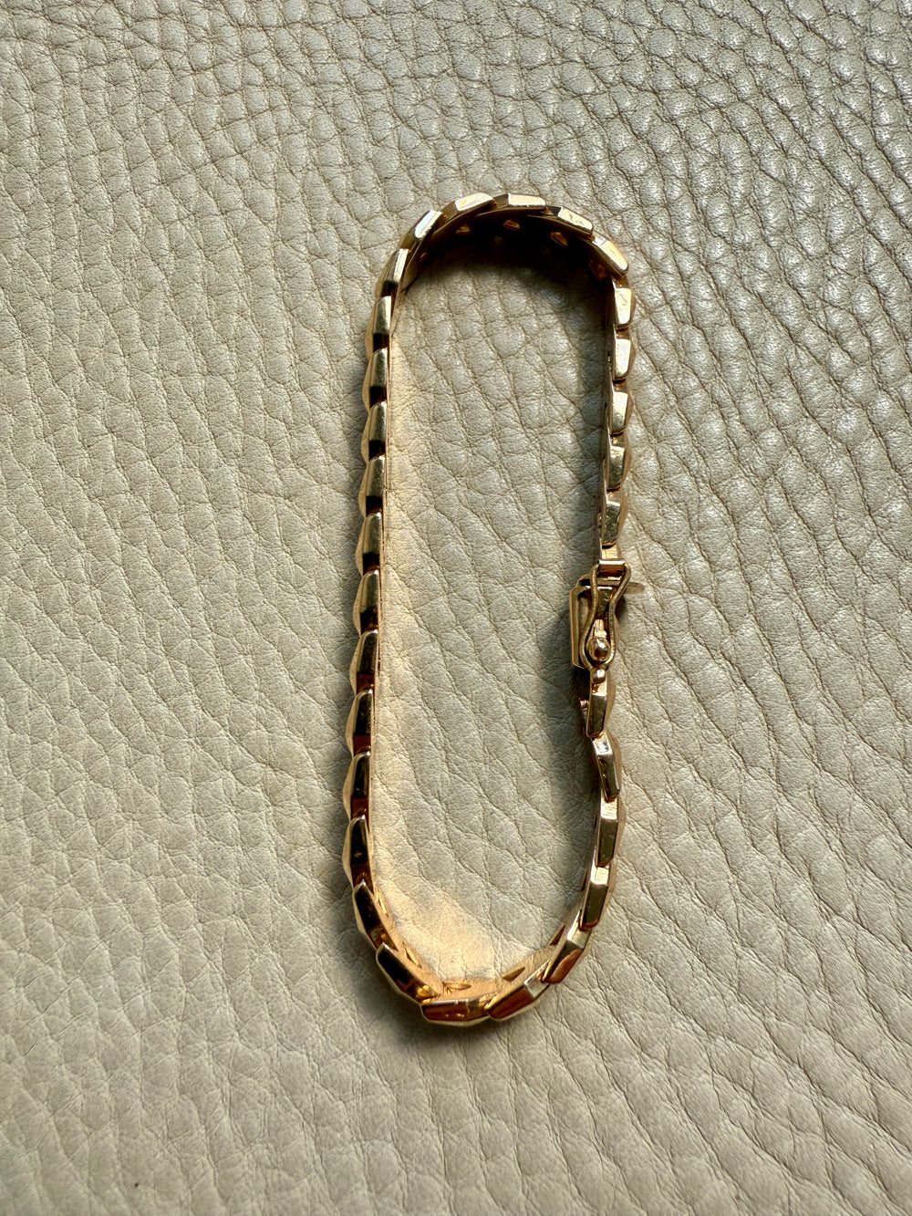 A vintage 18k gold link bracelet with a textured, segmented design, displayed on a light gray textured leather surface.