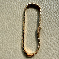 A vintage 18k gold link bracelet with a textured, segmented design, displayed on a light gray textured leather surface.