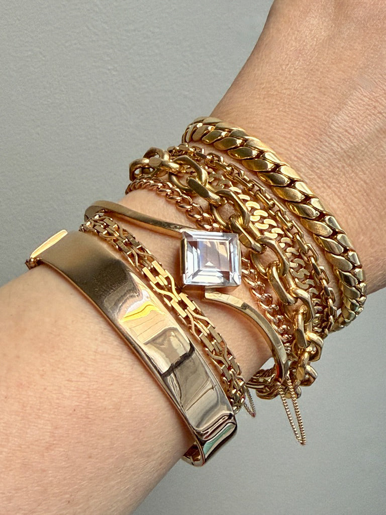 Gold bracelets with a clear gemstone on a wrist against a gray background. PenelopePenelope.com