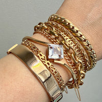 Gold bracelets with a clear gemstone on a wrist against a gray background. PenelopePenelope.com