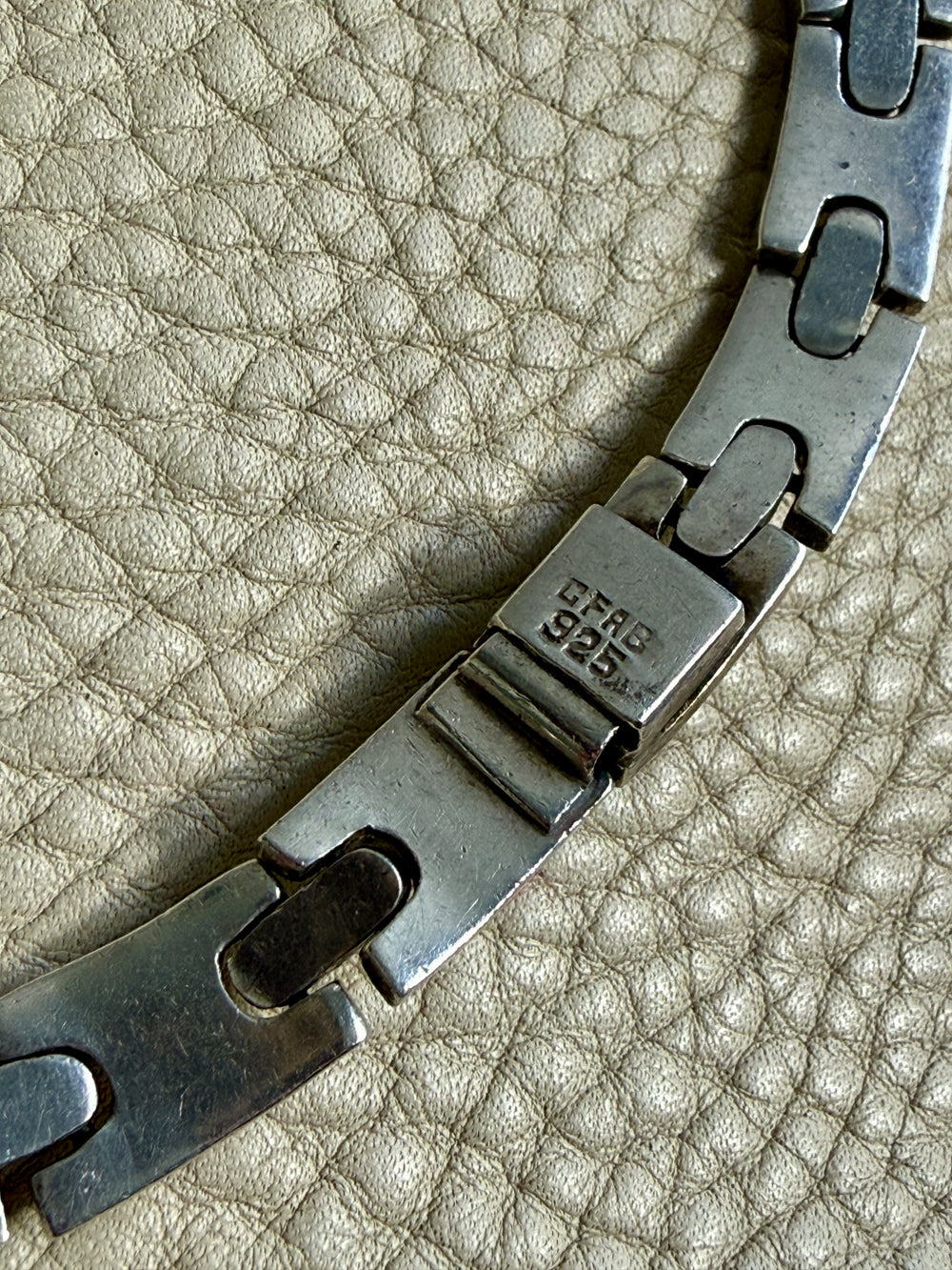 Close-up of a metal necklace clasp on a textured beige surface