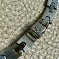 Close-up of a metal necklace clasp on a textured beige surface