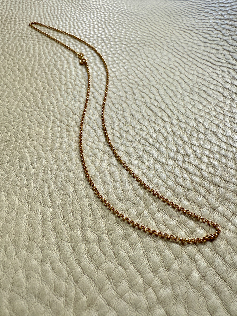 Gold chain necklace on a textured beige surface
