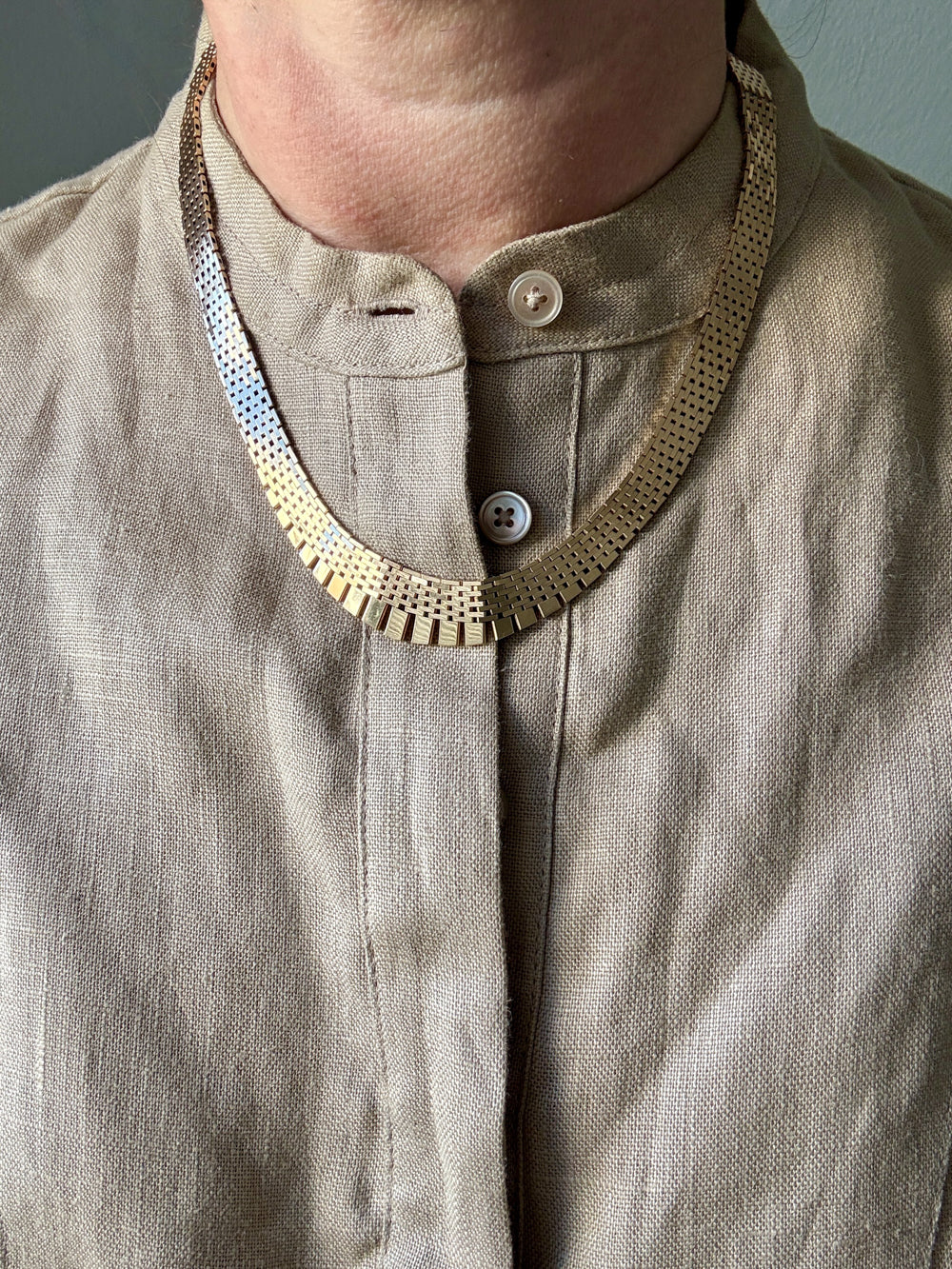 Close-up of a beige shirt with a 14k gold vintage cleopatra necklace and button details.