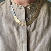 Close-up of a beige shirt with a 14k gold vintage cleopatra necklace and button details.