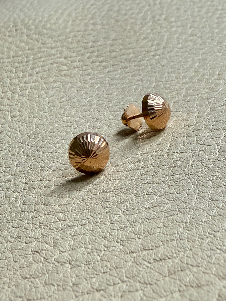Gold stud earrings on a light gray textured surface