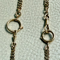 Two gold chain necklaces with clasp mechanisms on a light green textured background.