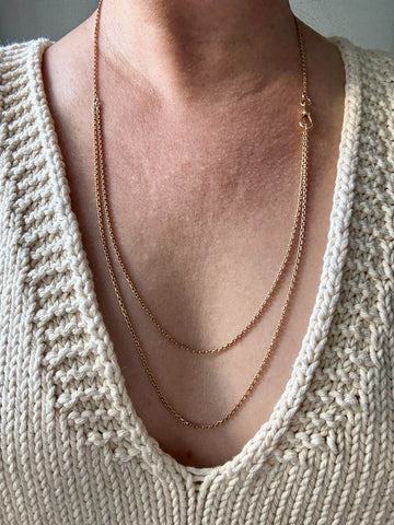 Close-up of a person wearing a gold necklace with a beige knitted sweater. Penelope Penelope vintage 18k gold fine jewelry