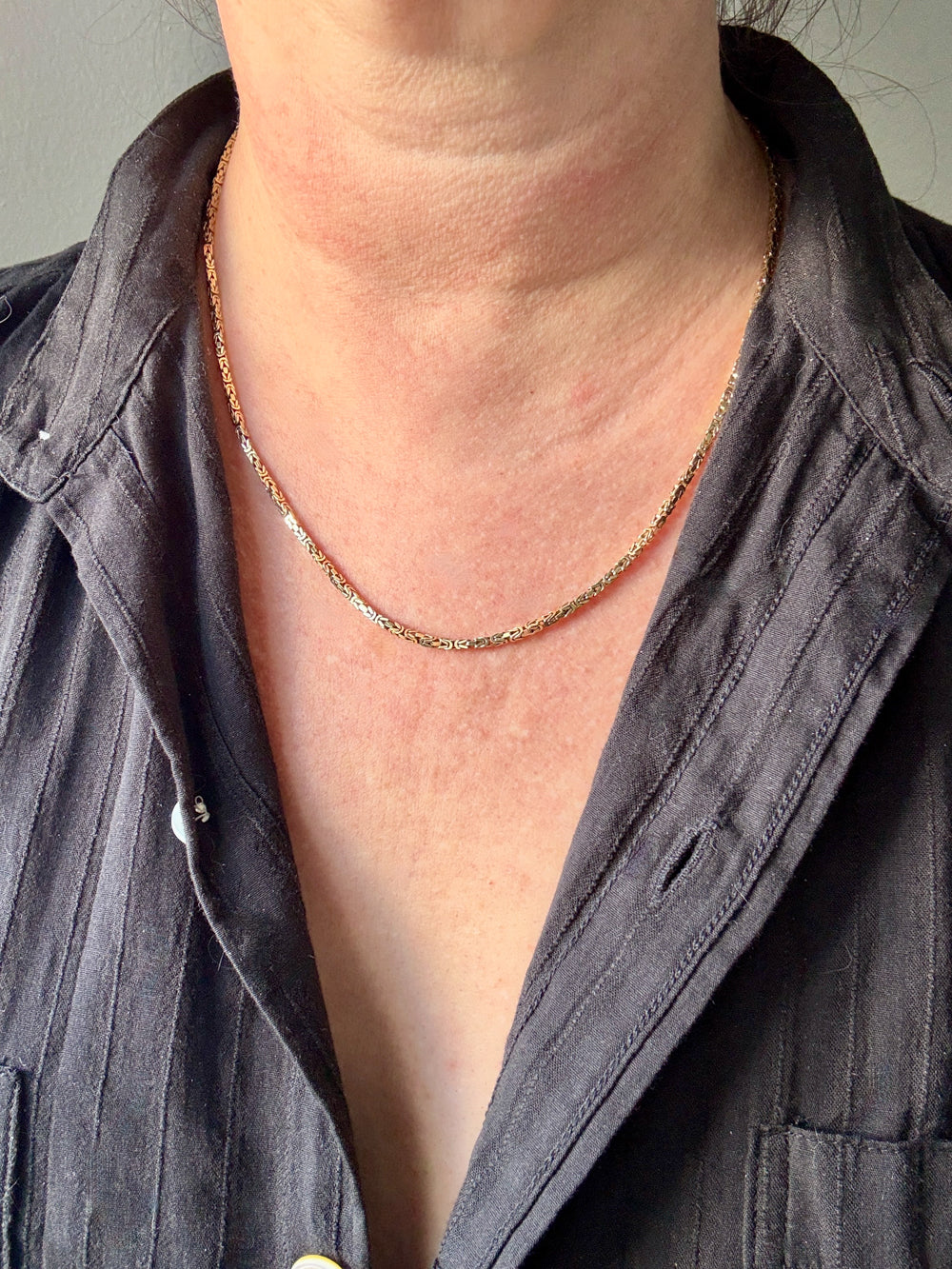 Person wearing a gold necklace with a plain background