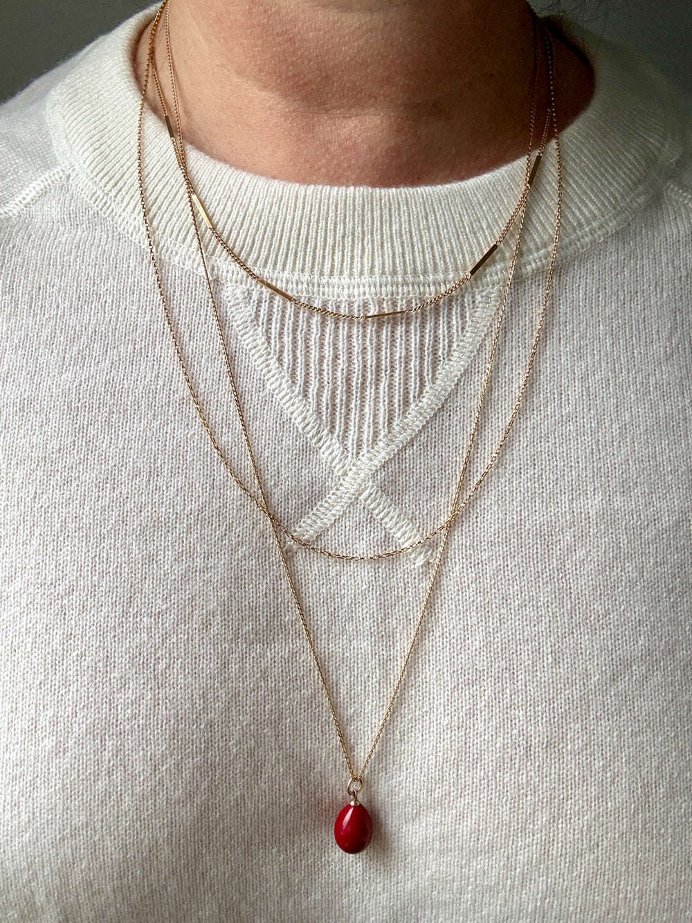 Necklaces with a red pendant worn by a person on a light gray background