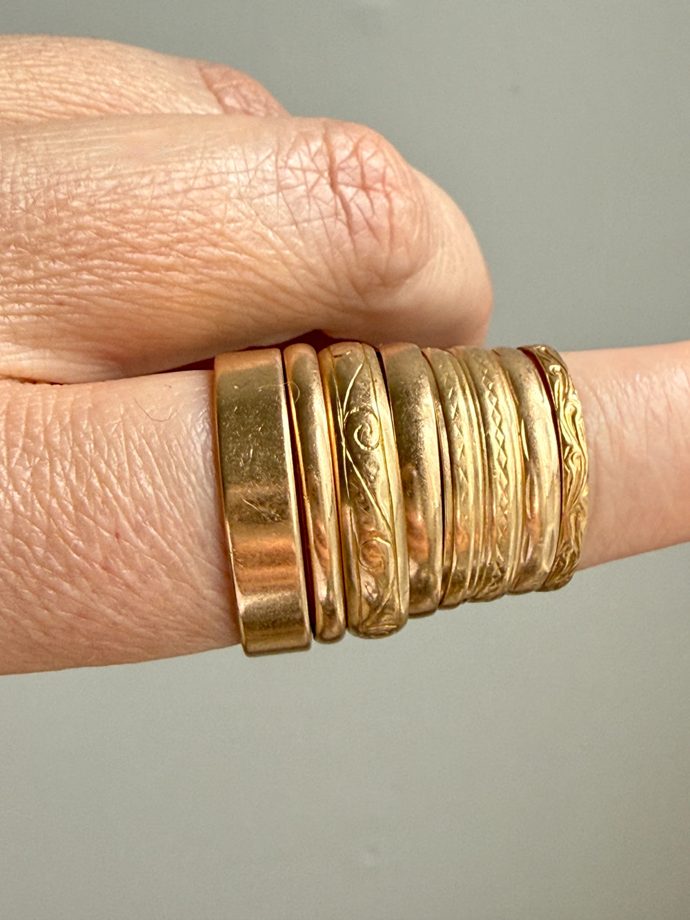 18k Gold rings with intricate designs on a finger against a neutral background