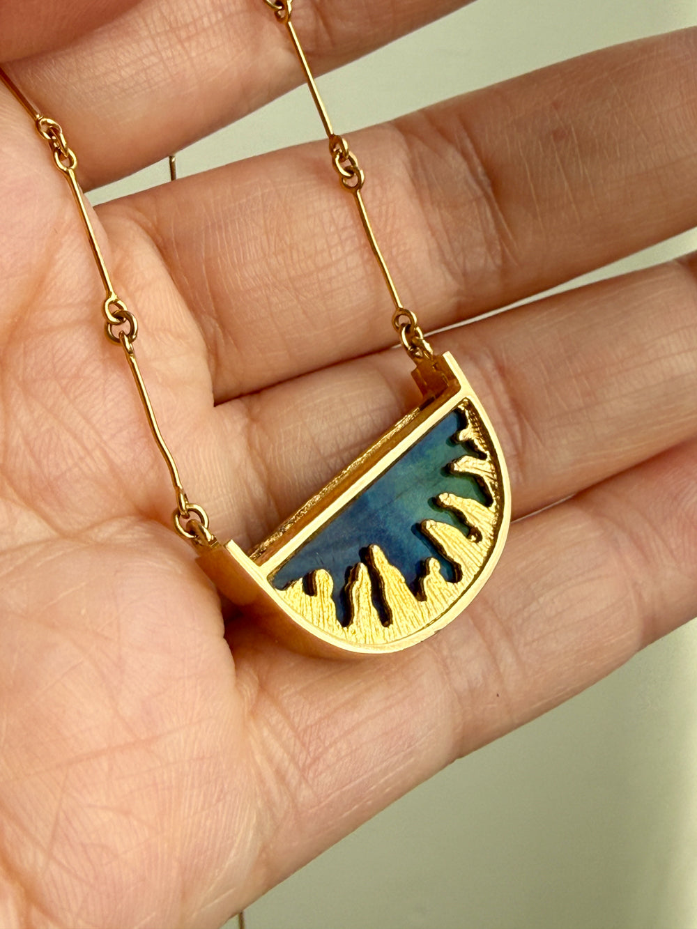 18k Gold necklace with a blue spectrolite pendant held in a hand against a neutral background