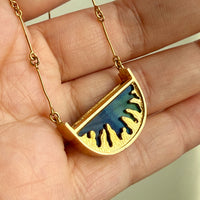 18k Gold necklace with a blue spectrolite pendant held in a hand against a neutral background