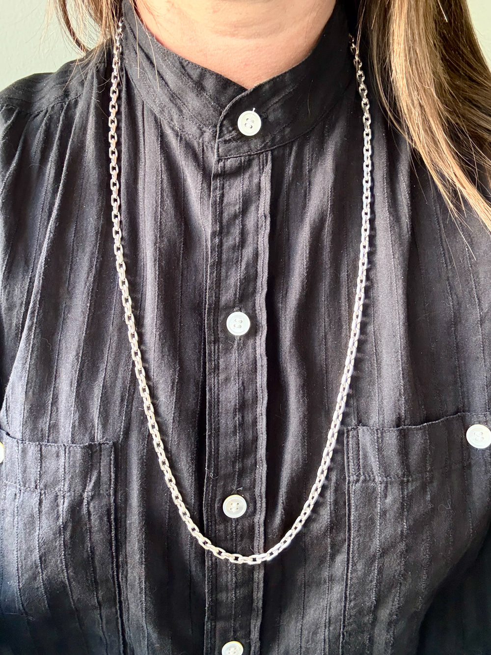 Person wearing a long silver chain necklace on a dark shirt.