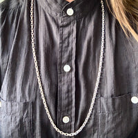 Person wearing a long silver chain necklace on a dark shirt.