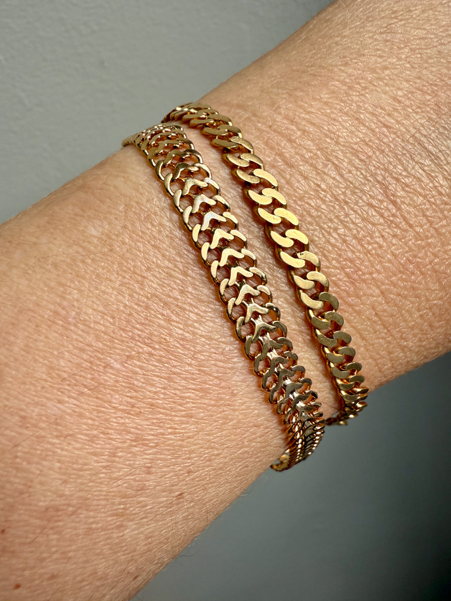 Gold chain bracelet on a wrist with a neutral background
