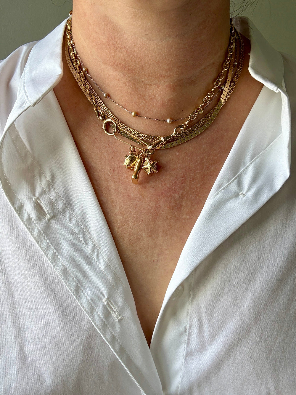Gold necklace with charms on a person wearing a white shirt.