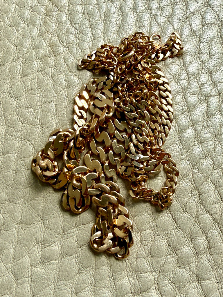 An 18k gold pressed curb link chain necklace draped across a textured light beige leather surface.
