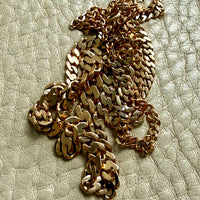 An 18k gold pressed curb link chain necklace draped across a textured light beige leather surface.