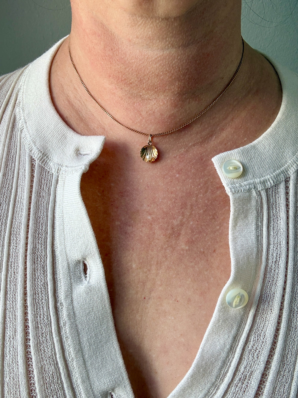 Close-up of a person wearing a white shirt with a necklace featuring a shell pendant.