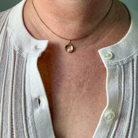 Close-up of a person wearing a white shirt with a necklace featuring a shell pendant.