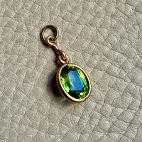 Gold pendant with a green peridot gemstone on a textured beige background