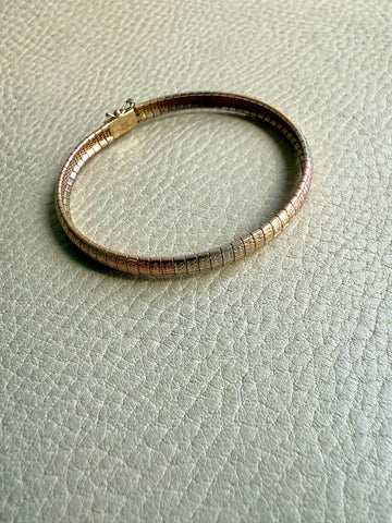 Gold tricolor bracelet on a light gray textured surface