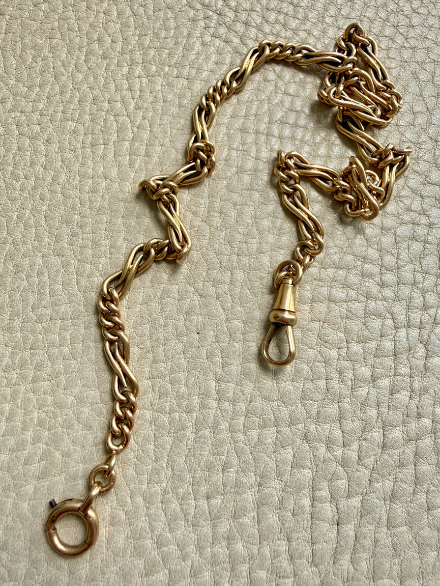 a french antique watch chain necklace in 18k gold displayed on a textured off-white surface.