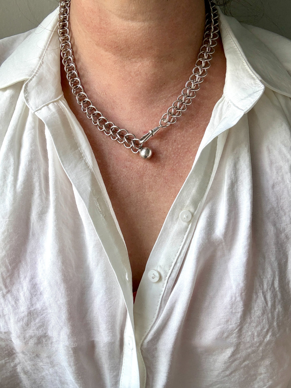 Person wearing a silver chain necklace with a white shirt.