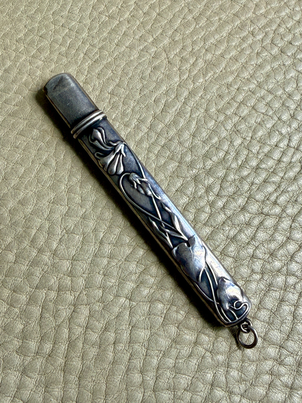 Silver art nouveau pencil case with intricate designs on a textured beige surface