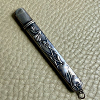 Silver art nouveau pencil case with intricate designs on a textured beige surface