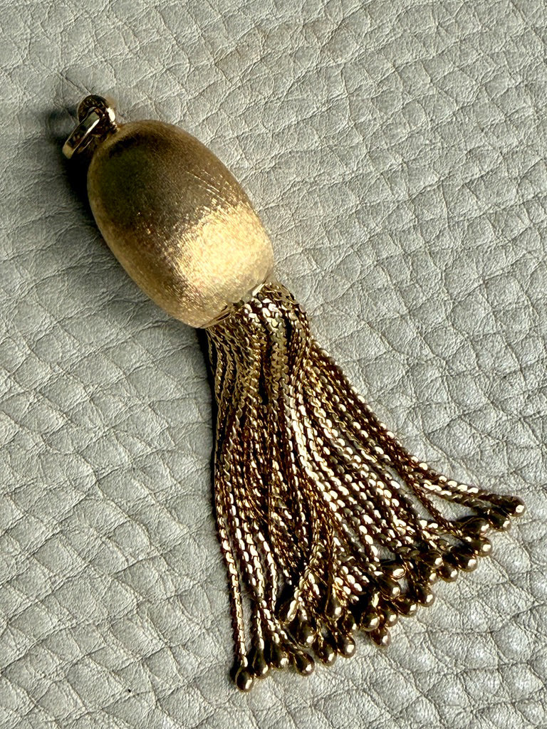 Gold tassel pendant on a textured light gray background