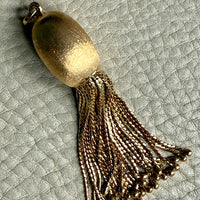 Gold tassel pendant on a textured light gray background
