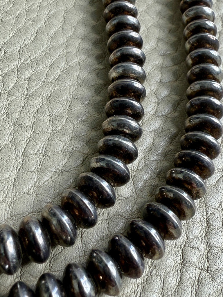 Close-up of a string of silver Navajo pearls on a textured gray background