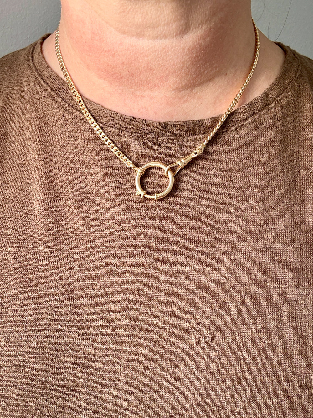 A close-up of a person wearing an 18k gold watch chain necklace paired with a brown knit top.